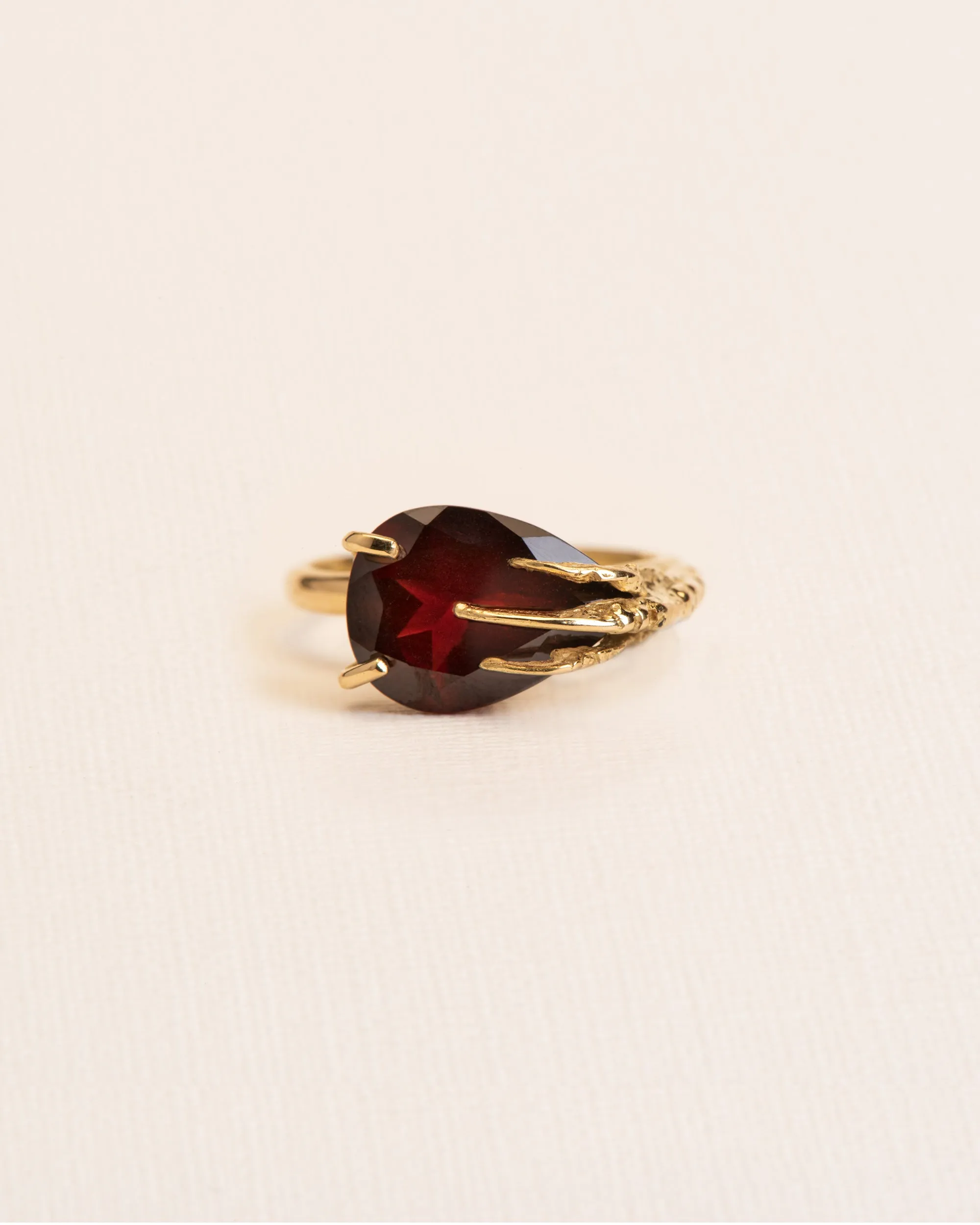 Signature grigri ring clasping a garnet in 18 ct. gold